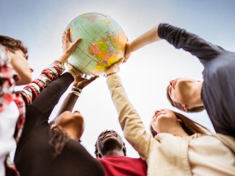 Students together holding a globe up to the sky